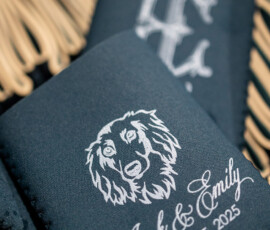 Dark drink sleeve with dog illustration, “Jack & Emily,” and 3/15/25 in white; ornate monogram sleeve in background.
