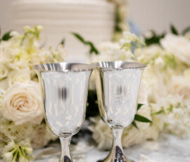 Silver goblets, white rose petals, and a white cake with blue hydrangeas create an elegant Louisiana wedding scene.