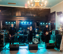 Wedding band with female vocalist and full ensemble performs on a lit stage, accented by flowers and spotlights.
