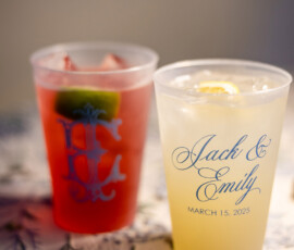 Two plastic cups on a floral tablecloth—one red with lime, one yellow, labeled Jack & Emily, March 15, 2025 in blue script.