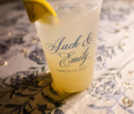 Plastic cup with lemon slice and light drink on floral tablecloth, reading “Jack & Emily, March 15, 2025” in elegant script.