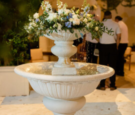 White stone fountain with floral arrangement, water, and soft lights above—an elegant Gulf South wedding scene.