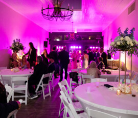 Louisiana wedding reception with round tables, white chairs, florals, and guests dancing under purple lights in a banquet hall.