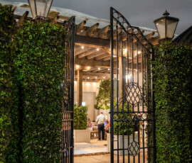 Wrought-iron gate with ivy and lanterns opens to pergola-lit wedding reception, evoking classic Louisiana charm.