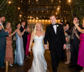 Bride and groom walk hand in hand, smiling as wedding guests with sparklers celebrate their nighttime Louisiana exit.