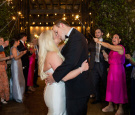 Bride and groom kiss as guests cheer and hold sparklers under string lights at a magical New Orleans wedding reception.