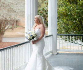 Bride in white strapless gown on porch with bouquet, surrounded by columns and greenery at a classic New Orleans wedding.