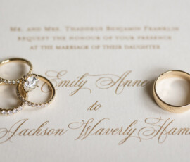 Three gold rings, including one with diamonds, on an elegant wedding invitation for Emily Anne and Jackson Waverly.