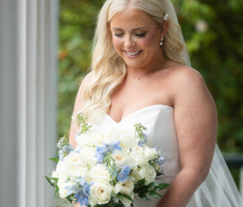 Bride in white strapless dress, smiling with a white and light blue bouquet, outdoors at a Louisiana wedding.