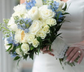 Bride’s torso in white dress holding a bouquet of white roses, light blue flowers, and greenery—Gulf South wedding inspiration.