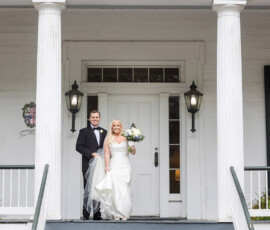 Bride in white dress and groom in black tuxedo smile on steps of classic white New Orleans wedding venue with columns and lanterns.