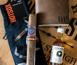 Men’s gift set with patterned socks, cigar, leather flask with BF initials, and Skrewball whiskey on wood—Louisiana wedding idea.