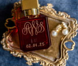 Red perfume bottle with gold details and pearl earrings on ornate tray, styled for a Gulf South wedding on blue fabric.