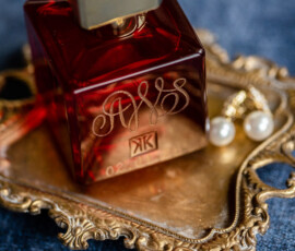 Red perfume bottle with gold details on a tray beside pearl earrings on blue—New Orleans wedding inspiration.
