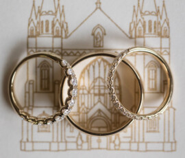 Three gold rings, two with diamonds, rest on a gold line church drawing—elegant Gulf South wedding inspiration.
