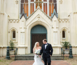 Bride and groom smiling outside an ornate church with arched windows and a brick walkway, perfect for classic Louisiana weddings.