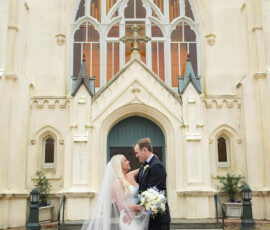 Bride and groom smile at each other outside an ornate church, capturing a classic Louisiana wedding moment.