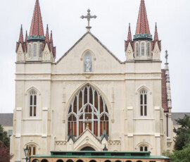 A green and beige trolley bus in front of an ornate church with tall spires, perfect for a New Orleans wedding backdrop.