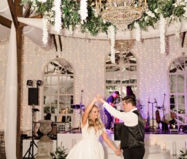 Bride and groom dance under a floral chandelier at their New Orleans wedding, with string lights and live band in the background.