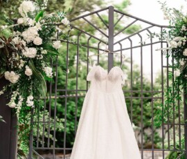 White wedding dress on a metal gate with green leaves and white flowers, New Orleans wedding inspiration in lush surroundings.