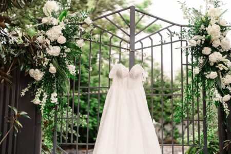 White wedding dress on a metal gate with green leaves and white flowers, New Orleans wedding inspiration in lush surroundings.
