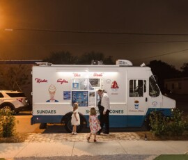 A night-lit ice cream truck serves a man and two girls at a Louisiana wedding, with plants lining the sidewalk.