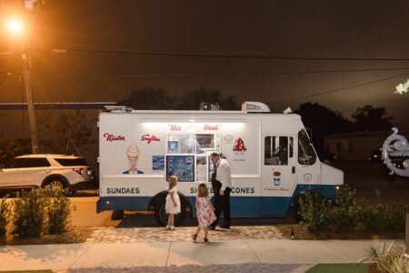 A night-lit ice cream truck serves a man and two girls at a Louisiana wedding, with plants lining the sidewalk.