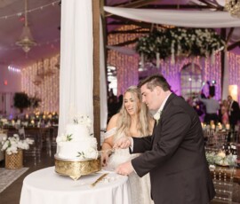 Bride and groom happily cut their white wedding cake at a decorated Louisiana reception with guests and twinkling lights.