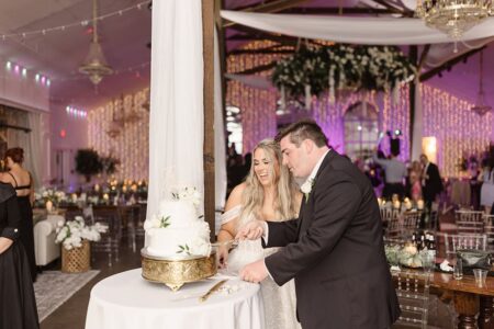 Bride and groom happily cut their white wedding cake at a decorated Louisiana reception with guests and twinkling lights.