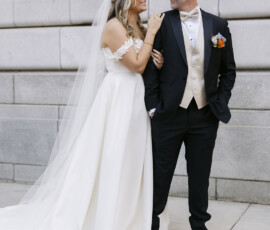 Couple standing together against a stone building wall during wedding portraits.