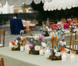 Outdoor wedding reception table with colorful garden-style flowers and candles beneath white scalloped umbrellas.