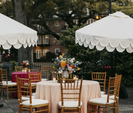 Courtyard reception tables with pastel linens, gold chiavari chairs, and floral centerpieces under string lights.