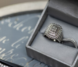 Square diamond ring with intricate band in gray box on glass, cursive background—ideal Louisiana wedding inspiration.