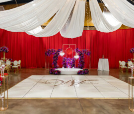 Ballroom with white drapes, string lights, red curtains, florals, white chairs, and gold-lettered dance floor—ideal Louisiana wedding.