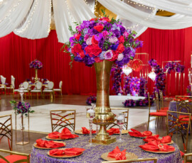Elegant round table with red napkins, gold vase of colorful flowers, in New Orleans wedding venue with draped white and red decor.