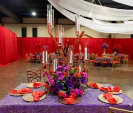 Elegant banquet table with purple cloth, red napkins, and gold settings in a hall with red drapes—ideal for New Orleans weddings.