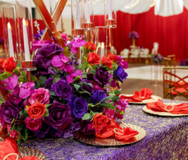 Elegant table set with purple and red flowers, gold plates, red napkins, and tall candles—ideal for a New Orleans wedding.