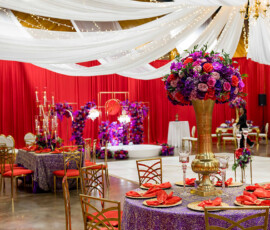New Orleans wedding reception with red and purple flowers, string lights, gold chairs, and elegantly set tables.