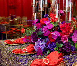Louisiana wedding table with red, purple, and pink flowers, gold accents, and elegant decor on a purple tablecloth.