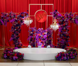 Elegant red curtains, chandeliers, and vibrant florals frame a white platform with a W² sign—stunning Louisiana wedding stage.