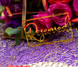 Gold Reserved sign on a purple and gold tablecloth with red and purple flowers, evoking New Orleans wedding elegance.