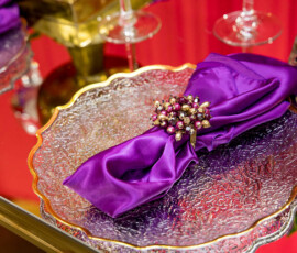 Gold-rimmed glass plate with a folded purple napkin and jeweled ring on a mirrored table—elegant New Orleans wedding detail.
