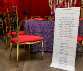 New Orleans wedding with gold chair, memorial scroll for loved ones, red cushions, and purple floral table coverings.