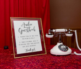 Vintage white rotary phone on red lace tablecloth with Audio Guestbook sign, red curtain backdrop—unique Gulf South wedding inspiration.