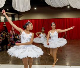 Three young ballerinas in white tutus dance at a New Orleans wedding, captivating guests before red curtains.