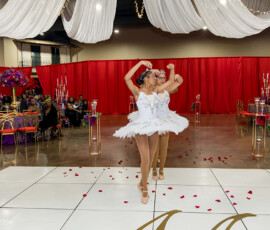 Three ballerinas in white tutus dance on a rose-petal floor at an elegant Louisiana wedding with red drapes and gold candelabras.