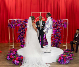 Bride and groom wed on a round platform with floral arch, red drapes, and purple-red flowers at an elegant New Orleans ceremony.
