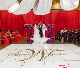 Bride and groom at wedding altar with bridesmaids in red, groomsmen in burgundy, surrounded by red drapes and floral decor.