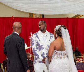 Bride and groom hold hands at their New Orleans wedding, with an officiant and red curtains in the background.