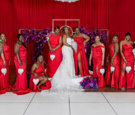 Bride in white gown with eleven bridesmaids in red dresses, holding white heart purses, at a New Orleans wedding.